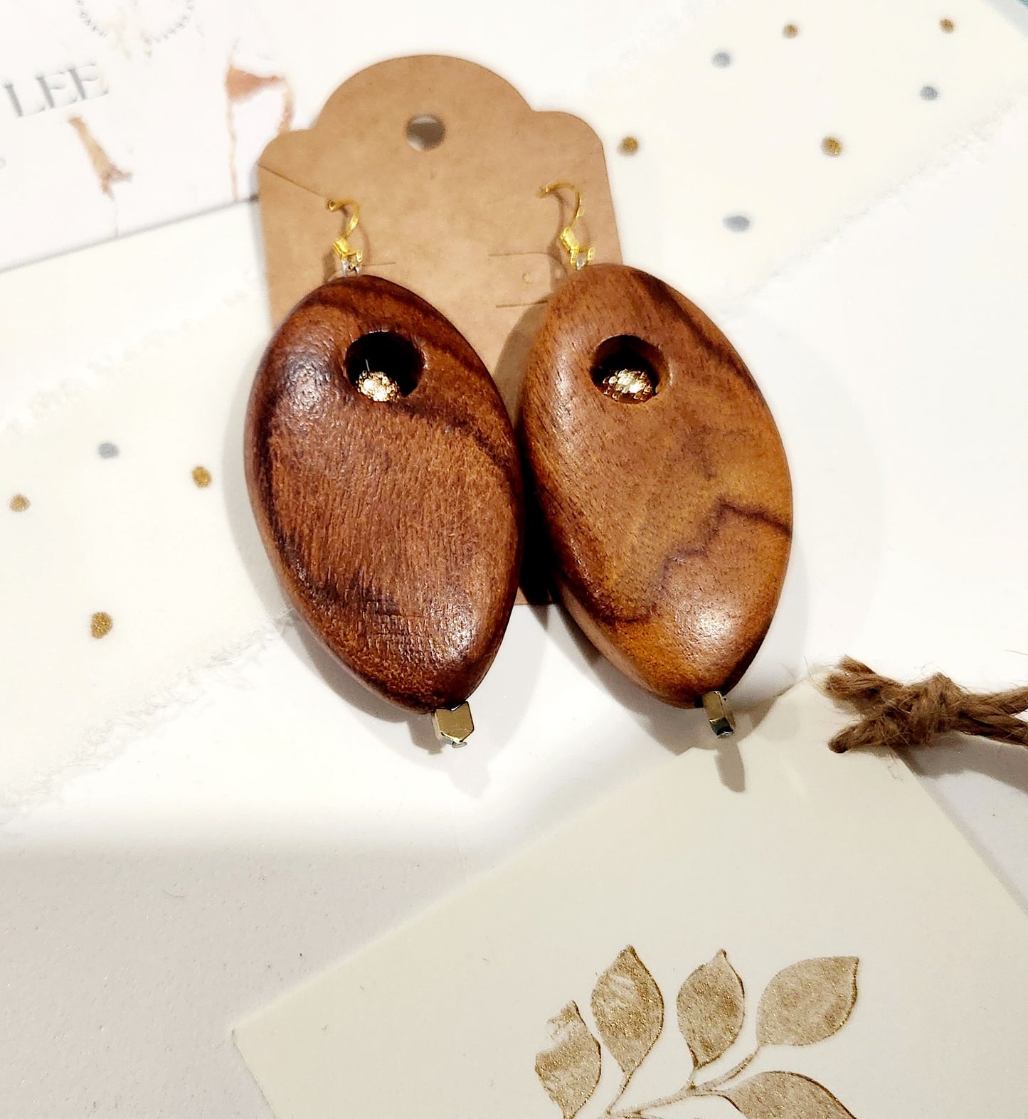 Handmade wooden earrings with gold-plated volcano stone bead, plated hematite accent, and 18K gold-plated sterling silver hooks on kraft card.
