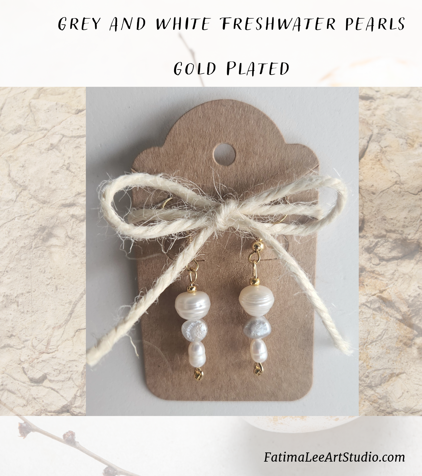 A pair of grey and white freshwater pearl earrings with gold-plated hooks, displayed on a beige card with a ribbon bow.