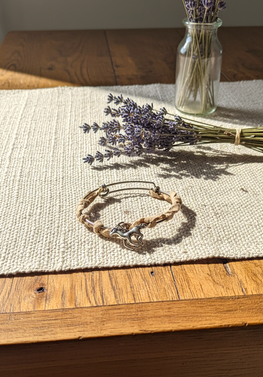 Handcrafted horse charm bracelet made with stainless steel, beige suede leather, and silver-plated horse pendant  on a wooden table with lavander flowers