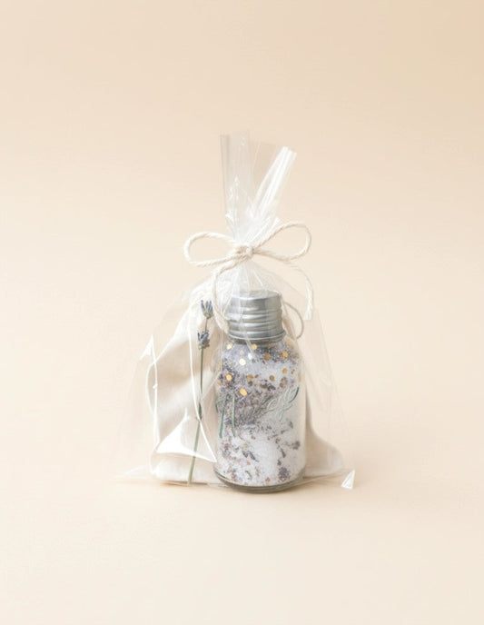 Decorative bottle with silver cap and floral design in a clear bag on a beige background