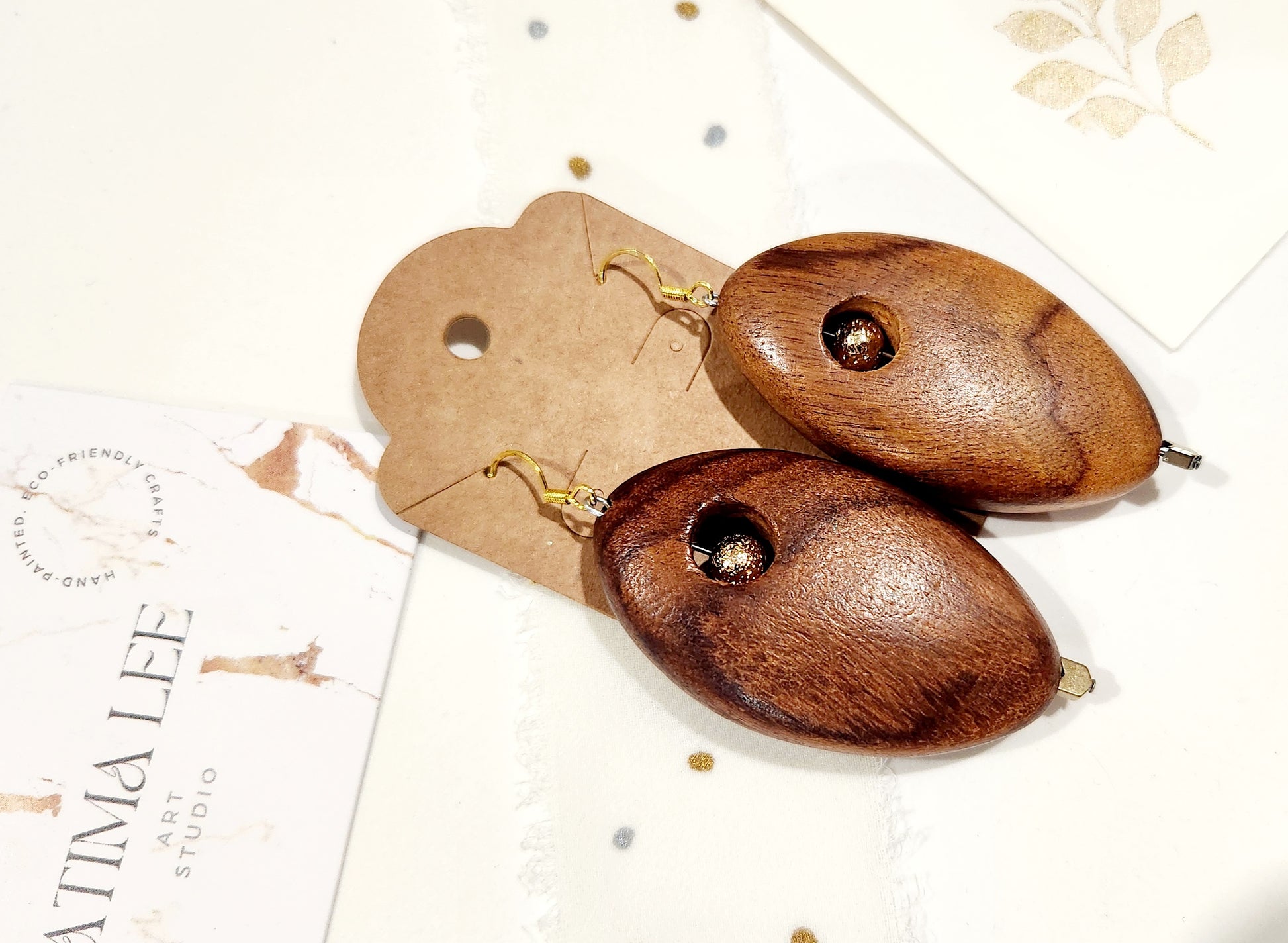 Handmade wooden earrings with gold-plated volcano stone bead, plated hematite accent, and 18K gold-plated sterling silver hooks on kraft card.
